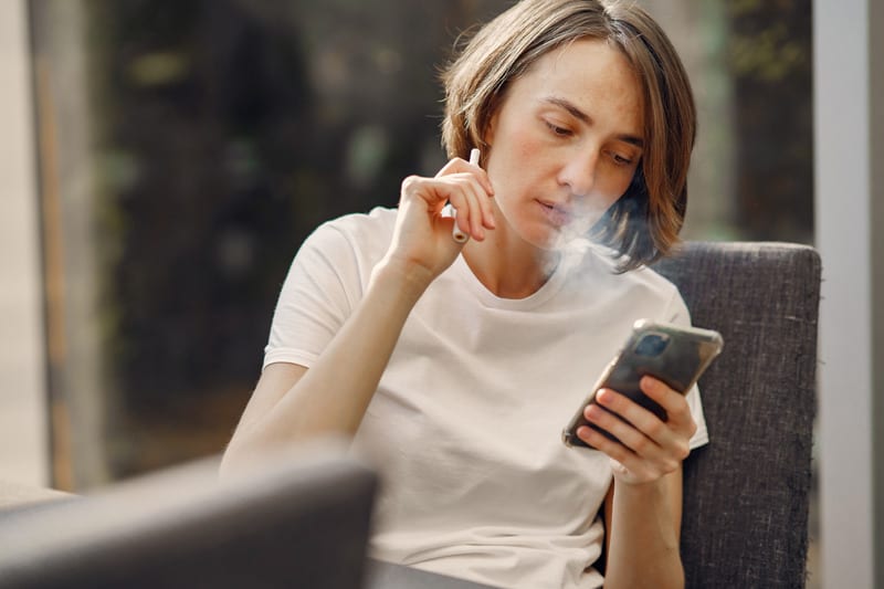Canva - Woman Smoking while Holding Her Phone